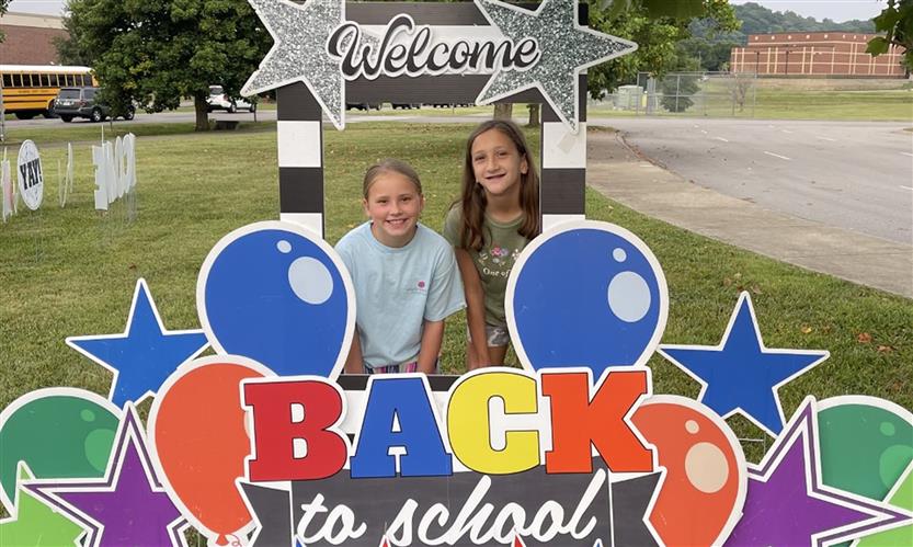 A group takes a photo with a welcome back sign